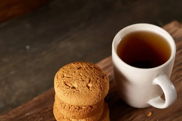 White porcelain mug of tea and sweet cookies on piece of wood over wooden background, top view, selective focus — Stock Photo, Image