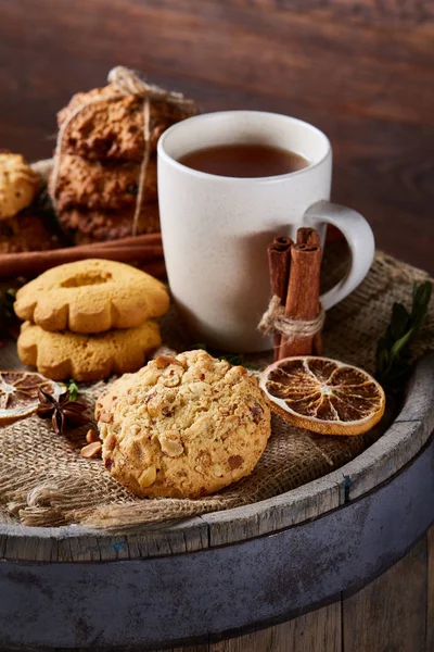 Konzeptionelle Festkomposition mit einer Tasse heißem Tee, Keksen und Gewürzen auf einem Holzfass, selektiver Fokus, vertikal — Stockfoto