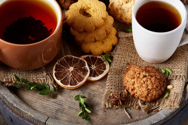 Conceptual festive composition with two cups of hot tea, cookies and spicies on wooden barrel, selective focus, close-up