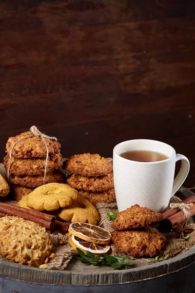 Konzeptionelle Festkomposition mit einer Tasse heißem Tee, Keksen und Gewürzen auf einem Holzfass, selektiver Fokus, Nahaufnahme — Stockfoto