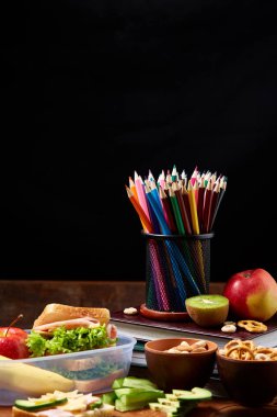 Okul öğle yemeği molası ile sağlıklı öğle yemeği kutusu ve okul malzemeleri ahşap masa, seçici odak kavramı.