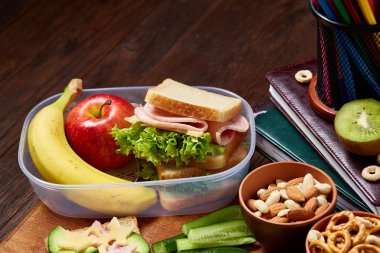 Okul öğle yemeği molası ile sağlıklı öğle yemeği kutusu ve okul malzemeleri ahşap masa, seçici odak kavramı.