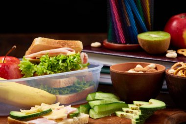 Okul öğle yemeği molası ile sağlıklı öğle yemeği kutusu ve okul malzemeleri ahşap masa, seçici odak kavramı.