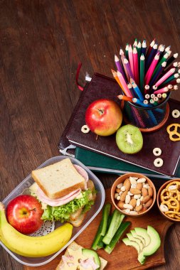 Okul öğle yemeği molası ile sağlıklı öğle yemeği kutusu ve okul malzemeleri ahşap masa, seçici odak kavramı.