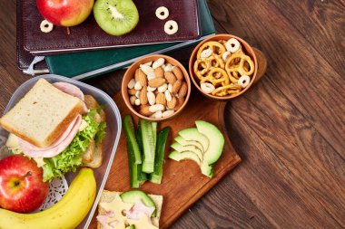 Okul öğle yemeği molası ile sağlıklı öğle yemeği kutusu ve okul malzemeleri ahşap masa, seçici odak kavramı.