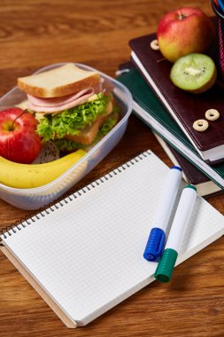 Okul öğle yemeği molası ile sağlıklı öğle yemeği kutusu ve okul malzemeleri ahşap masa, seçici odak kavramı.