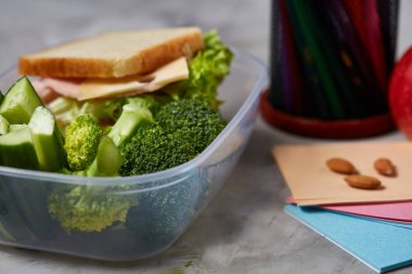 Yeşil salata ve konteyner ve okul malzemeleri, beyaz masa, seçici odak üzerinde sebze ile lezzetli öğle yemeği.