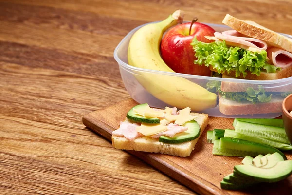 Okul veya sandviç ile öğle yemeği kutusu ve çeşitli renkli sebze ve meyve ahşap arka plan üzerinde piknik, yakın çekim.