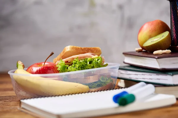 Concetto di pausa pranzo scolastica con pranzo sano e materiale scolastico su scrivania in legno, focus selettivo . — Foto Stock