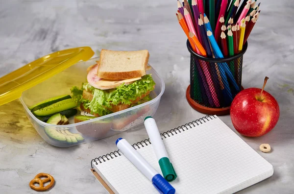 Concetto di pausa pranzo scolastica con pranzo sano e materiale scolastico sulla scrivania bianca, focus selettivo . — Foto Stock