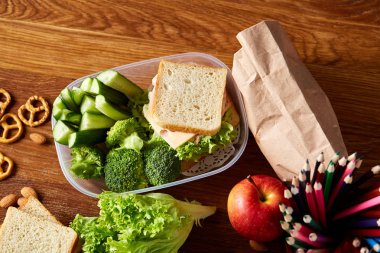 Okul öğle yemeği molası ile sağlıklı öğle yemeği kutusu ve okul malzemeleri ahşap masa, seçici odak kavramı.