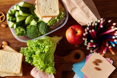 Okul öğle yemeği molası ile sağlıklı öğle yemeği kutusu ve okul malzemeleri ahşap masa, seçici odak kavramı.