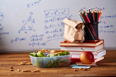 Geri okul kavramı, okul malzemeleri, bisküvi, paket öğle yemeği ve beslenme çantası beyaz yazı tahtası, seçici odak üzerinde.