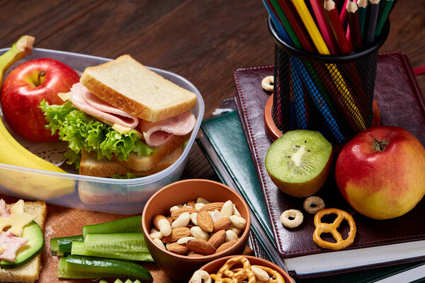 School or picnic lunch box with sandwich and various colorful vegetables and fruits on wooden background, close up.