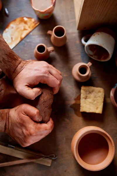 Close-up hands of a male potter in apron molds bowl from clay, selective focus