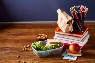 Okul öğle yemeği molası ile sağlıklı öğle yemeği kutusu ve okul malzemeleri ahşap masa, seçici odak kavramı.