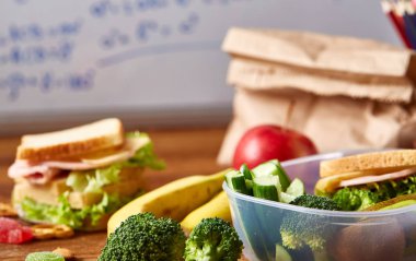 Geri okul kavramı, okul malzemeleri, bisküvi, paket öğle yemeği ve beslenme çantası beyaz yazı tahtası, seçici odak üzerinde.