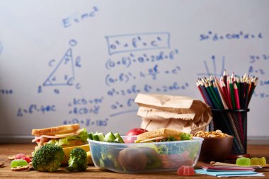 Geri okul kavramı, okul malzemeleri, bisküvi, paket öğle yemeği ve beslenme çantası beyaz yazı tahtası, seçici odak üzerinde.
