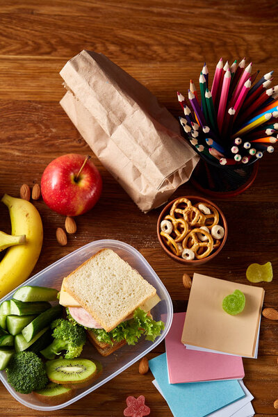Concept of school lunch break with healthy lunch box and school supplies on wooden desk, selective focus.