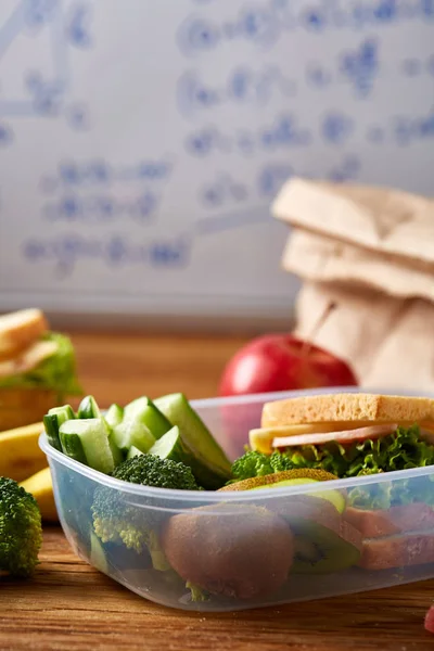 Concetto di rientro a scuola, forniture scolastiche, biscotti, pranzo al sacco e cestino per il pranzo sulla lavagna bianca, focus selettivo . — Foto Stock