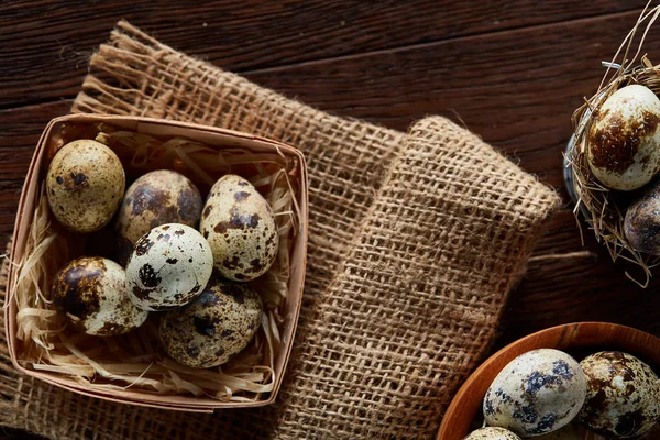 Rustic still life with quail eggs in bucket, box and bowl on a linen napkin over wooden background, selective focus — Stock Photo, Image