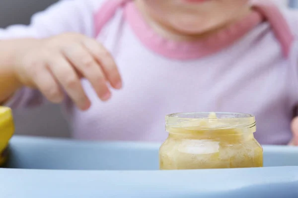 Criança na cozinha comendo purê de frutas, profundidade de campo rasa, foco seletivo . — Fotografia de Stock