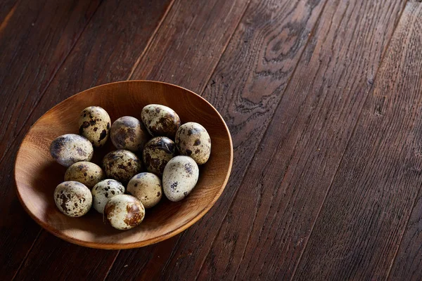 Huevos frescos de codorniz en un plato de madera sobre un fondo de madera oscura, vista superior, primer plano — Foto de Stock