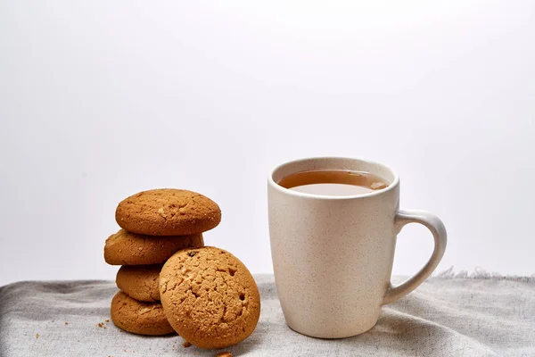 White porcelain mug of tea and sweet cookies on homespun napkin over white background, top view, selective focus — Stock Photo, Image