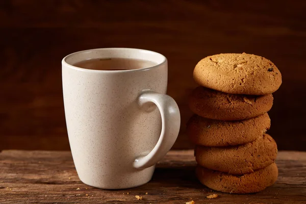 White porcelain mug of tea and sweet cookies on piece of wood over wooden background, top view, selective focus — Stock Photo, Image