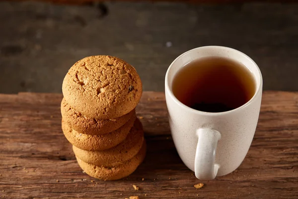 White porcelain mug of tea and sweet cookies on piece of wood over wooden background, top view, selective focus — Stock Photo, Image