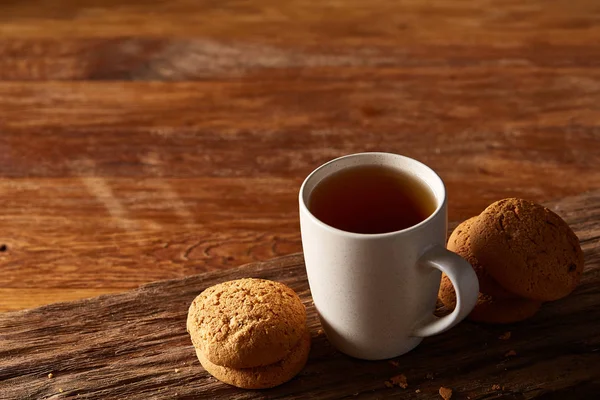 Taza de porcelana blanca de té y galletas dulces en pieza de madera sobre fondo de madera, vista superior, enfoque selectivo — Foto de Stock