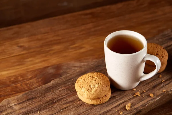 Caneca de porcelana branca de chá e biscoitos doces em pedaço de madeira sobre fundo de madeira, vista superior, foco seletivo — Fotografia de Stock