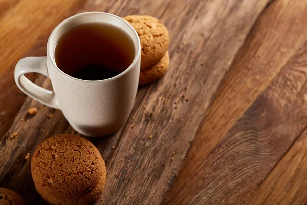 White porcelain mug of tea and sweet cookies on piece of wood over wooden background, top view, selective focus — Stock Photo, Image