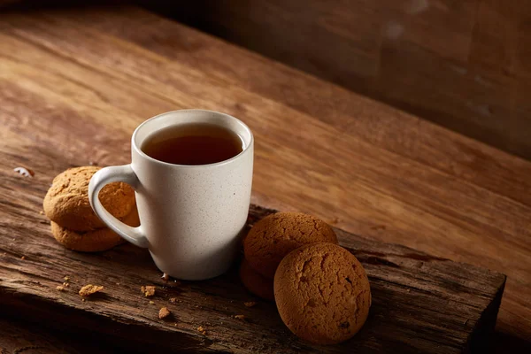 Caneca de porcelana branca de chá e biscoitos doces em pedaço de madeira sobre fundo de madeira, vista superior, foco seletivo — Fotografia de Stock