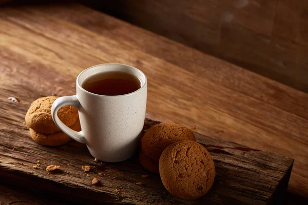 White porcelain mug of tea and sweet cookies on piece of wood over wooden background, top view, selective focus — Stock Photo, Image