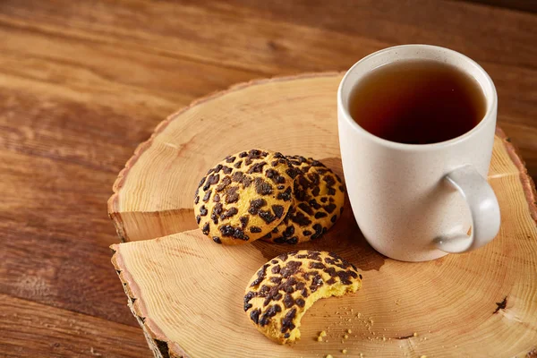 White cup of tea and cookies on a log over country style wooden background, close-up, selective focus