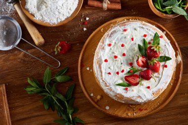 Çilekli tart ahşap arka plan üzerinde düz yatıyordu organik maddeler tarafından çevrili ekşi krem şanti ile kaplı.