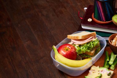 Okul öğle yemeği molası ile sağlıklı öğle yemeği kutusu ve okul malzemeleri ahşap masa, seçici odak kavramı.