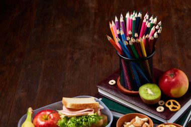 Okul öğle yemeği molası ile sağlıklı öğle yemeği kutusu ve okul malzemeleri ahşap masa, seçici odak kavramı.