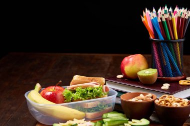 Okul öğle yemeği molası ile sağlıklı öğle yemeği kutusu ve okul malzemeleri ahşap masa, seçici odak kavramı.