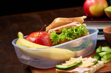 Okul öğle yemeği molası ile sağlıklı öğle yemeği kutusu ve okul malzemeleri ahşap masa, seçici odak kavramı.