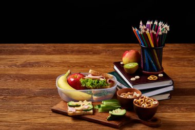 Okul öğle yemeği molası ile sağlıklı öğle yemeği kutusu ve okul malzemeleri ahşap masa, seçici odak kavramı.