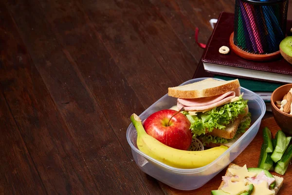 Okul öğle yemeği molası ile sağlıklı öğle yemeği kutusu ve okul malzemeleri ahşap masa, seçici odak kavramı.