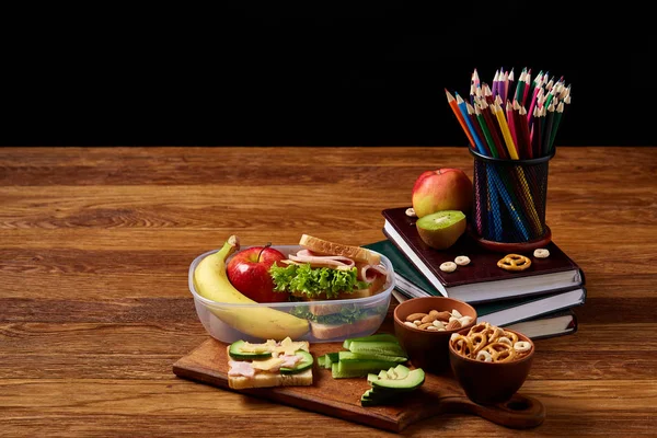 Okul öğle yemeği molası ile sağlıklı öğle yemeği kutusu ve okul malzemeleri ahşap masa, seçici odak kavramı.