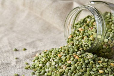 Saf masa örtüsü, yakın çekim, seçici odak devrilmiş cam kavanoza ham yeşil bezelye.