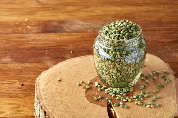 Raw green peas in glass jar on a log over wooden background, close-up, selective focus.
