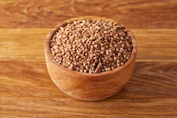 Bowl full of buckwheat grains on rustic wooden table, close-up, selective focus.