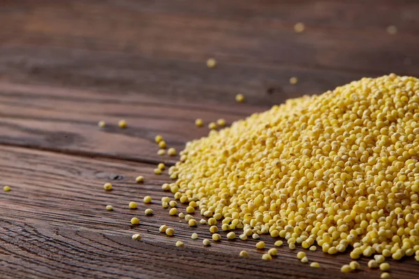 Pile of natural organic millet on rustic wooden background, top view, close-up, selective focus.