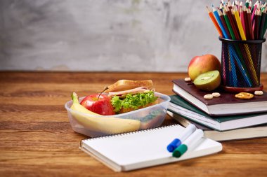Okul öğle yemeği molası ile sağlıklı öğle yemeği kutusu ve okul malzemeleri ahşap masa, seçici odak kavramı.