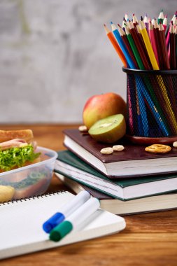 Okul öğle yemeği molası ile sağlıklı öğle yemeği kutusu ve okul malzemeleri ahşap masa, seçici odak kavramı.